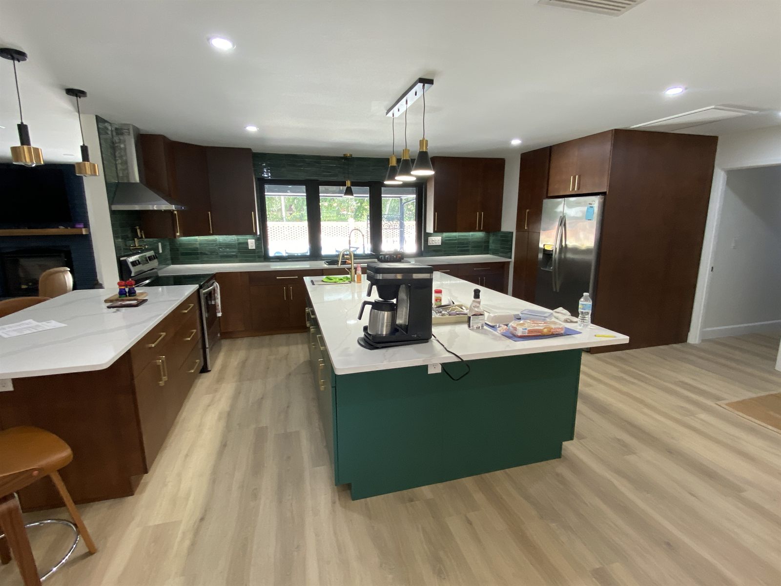 Finished kitchen remodel with green island, wood cabinetry, and gold pendant lighting
