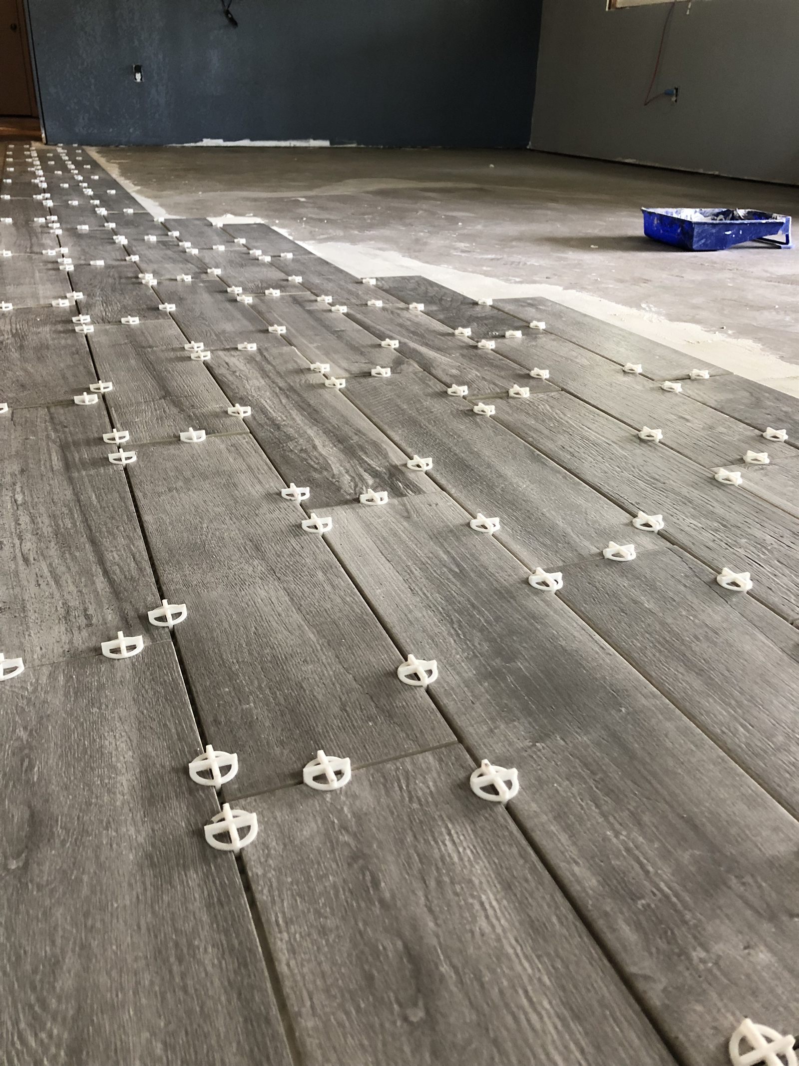 Wood-look floor tile mid-installation with leveling spacers, laid out with precision